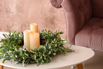 Obraz na płótnie Canvas Burning candles with wreath on table near pink armchair, closeup