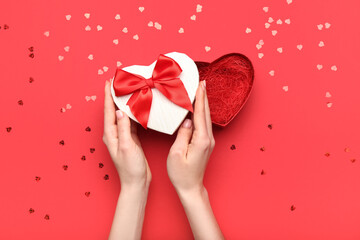 Female hands with gift box for Valentine's Day on red background