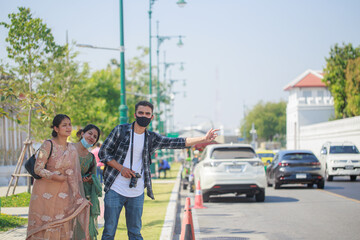 Three South Asian tourists with cameras happily hitchhiking the road behind Wat Pho during their long weekend happily. in Bangkok, Thailand
