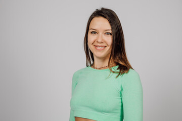 Obraz premium Portrait of smiling young woman. Beautiful happy brunette is smiling and posing on gray isolated background, she is wearing green jacket for yoga or fitness.