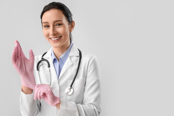 Portrait of female doctor putting on rubber gloves against grey background