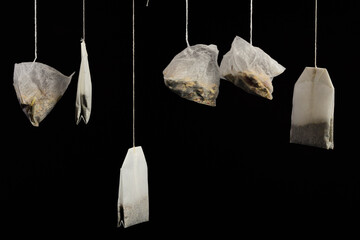 Close up of various tea bags hanging from above, against a dark background, with space for text