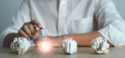 New idea and light bulb concept man hand touching light bulb with  crumpled office paper....