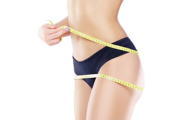 Young and fit female body close-up. Waist of beautiful and slender woman with measuring tape isolated on white. Sport, fitness, diet and healthy eating concepts.