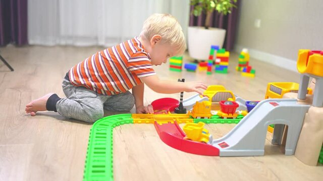 A blond boy is rolling a children's train along the rails of the railroad