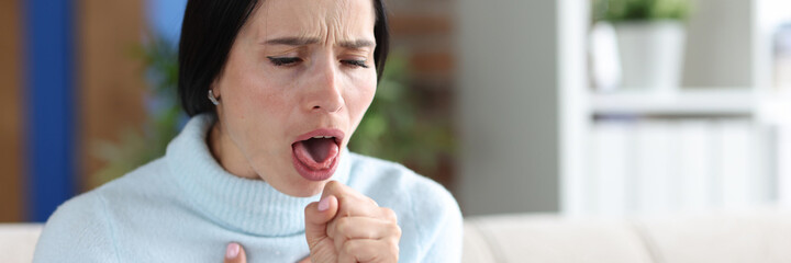 Woman with coughing fits sits on couch closeup