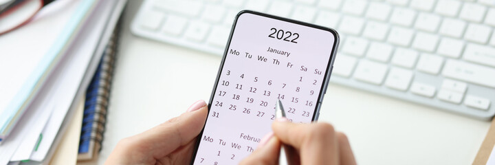 Smartphone on screen with calendar for 2022 pen in female hands