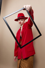 fashionable woman frame in hand in red hat and jacket beige background