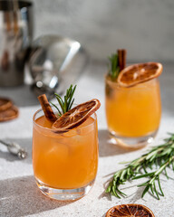 Alcoholic cocktail decorated with rosemary sprig, cinnamon stick and dried orange slice on light background