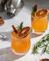 Alcoholic cocktail decorated with rosemary sprig, cinnamon stick and dried orange slice on light background