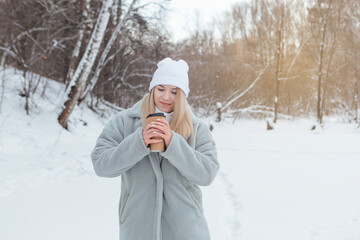 A beautiful young girl smiles and enjoys drinking coffee in a winter forest.