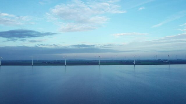 Drone truck shot of the lakeshore covered in wind turbines on a calm windless day.