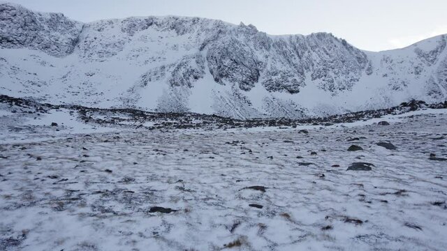 Rolling aerial drone footage close to the ground the headwall of Coire an t-Sneachda in the Cairngorm mountains of Scotland in snow, ice and full winter mountaineering conditions with snow and ice.