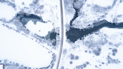 Aerial top down view of beautiful winter lanscape empty road crossing a frozen river. Snow landscape with fantastic winter pattern