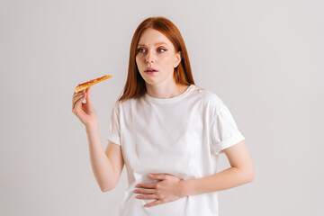 Studio portrait of sick upset young woman feeling pain in stomach after eating pizza, suffering...