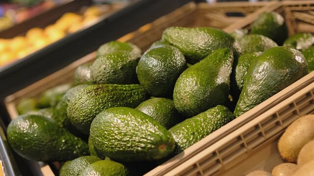 At the Supermarket: Close-up Shot of the Woman's Hand Taking Avocado from the Fresh Produce Section and Places it into Shopping Cart.