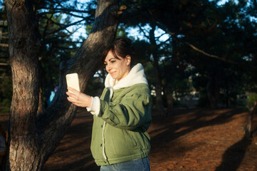 Smiling woman with mobile phone makes selfie in the forest