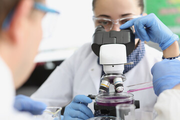 Female scientist explore purple sample under microscope in laboratory