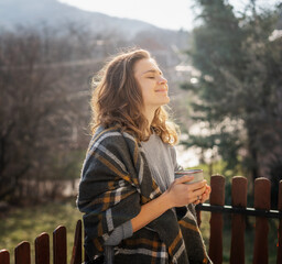 Happy cheerful beautiful curly young woman enjoying morning coffee and nature view on the terrace of a country house