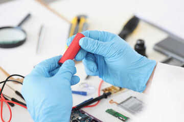 Male in blue gloves holding red battery piece, repairing broken or damaged device by himself