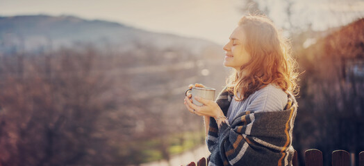 Happy cheerful beautiful curly young woman enjoying morning coffee and nature view on the terrace of a country house