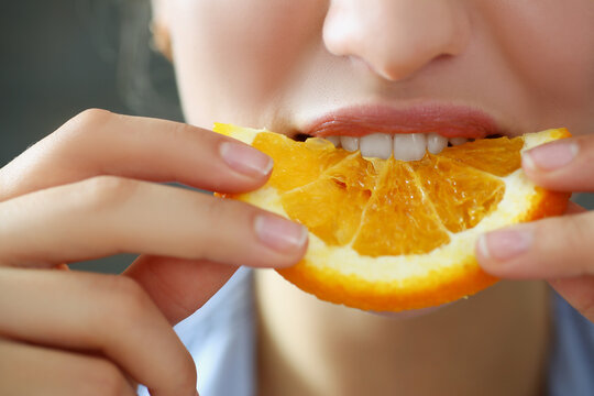 Woman hold in hand slice of chopped orange eats for breakfast with mouth in kitchen