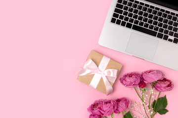Bouquet of flowers, laptop and gift box with tied bow on a pink background. Online dating concept, present for Mothers Day with place for text.
