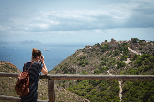 Young traveler girl with leather backpack taking a picture at the viewpoint