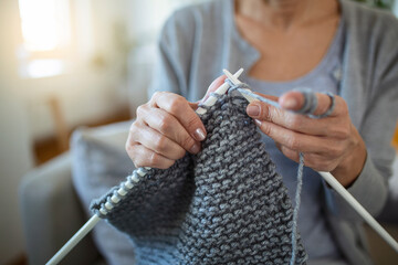 Close up view grandmother hands holding needles make repetitive motion knitting sitting on couch creating something with her arms. Hand knitting improve brain function, older generation hobby concept