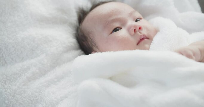 Portrait close up pretty Asian newborn baby infant girl in white bathrobe lying bed in a basket at home with eyes open, children, parenthood, childhood, life, maternity, love concept