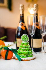 Gingerbread in the form of a Christmas tree with green glaze on a New Year's table against a background of champagne