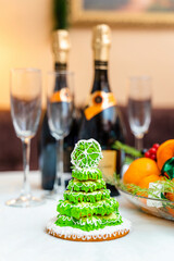 Gingerbread in the form of a Christmas tree with green glaze on a New Year's table against a background of champagne