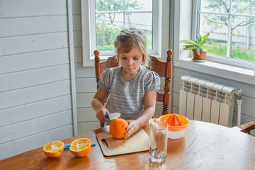 the child girl in the kitchen cuts and squeezes oranges juice
