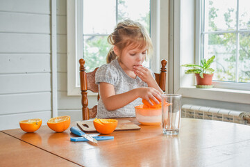 the child girl in the kitchen cuts and squeezes oranges juice