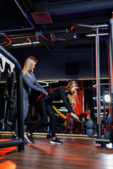 Obraz premium Sport, fitness, bodybuilding, lifestyle and workout concepts - woman doing sports under the strict guidance of a trainer in the gym, working on muscles in the gym