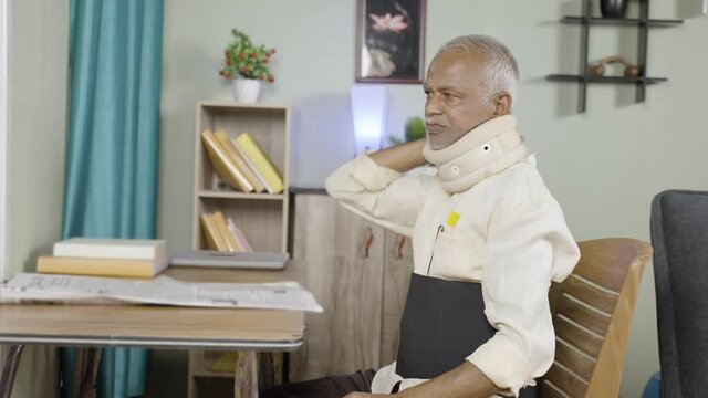 Sick senior with neck breace and waist support belt reading news paper at home - concept of senior suffering joint paint, unhealthy lifestyle and multiple joint injury.
