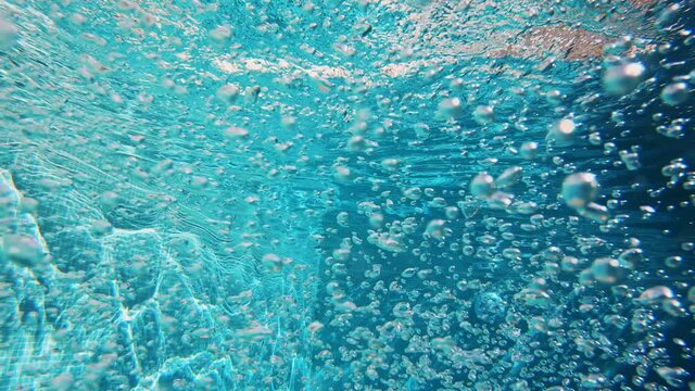 4K Cinematic slow-motion underwater footage. Lots of air bubbles float in the blue water of the pool.