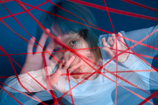 Young woman is entangled in red threads on blue walls background. Concept of obsessive states, paranoia, mental illness. Double exposure