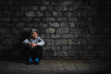 Fototapeta na wymiar Depressed hispanic teenager sitting against a wall in the darkness. Anxiety and depression in adoloscence concept.