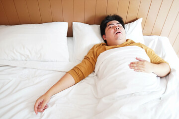 chubby asian man lay down on white bed and sleeping and snoring in morning light. authentic people....