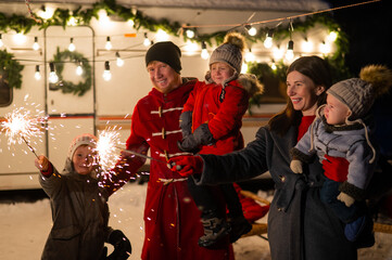 Obraz premium Happy family celebrates christmas in nature and holds sparklers. Parents with three sons travels in a van.