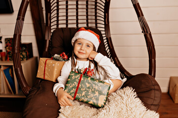 Smiling happy kid in Santa cap and white dress holding gift box and waiting for Christmas party