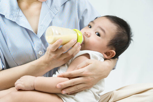 Mother feeding baby boy with milk in glass bottle in bed closeup. Good morning. Breakfast time. Healthy eating. Childhood.
