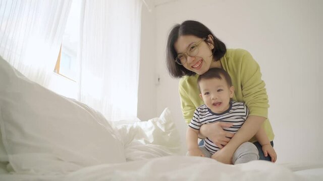 Loving Smiling Young Mother playing hugging her little baby boy on the bed, Happy Asian Mom and son, Human relationships, Mother's day concept 