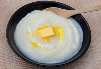 Traditional South African Maize meal porridge in a black bowl with block of butter on rustic...