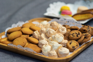  assorted cookies on a wooden plate. close-up. there is a wooden plate with three kinds of cookies on a table with a gray tablecloth. Chocolate chip cookies