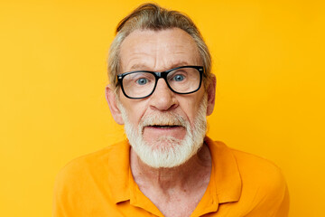 Senior grey-haired man wearing glasses yellow shirt posing isolated background