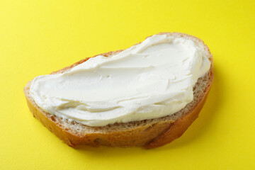 Slice of bread with tasty cream cheese on yellow background, closeup