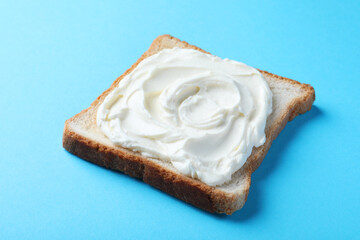 Slice of bread with tasty cream cheese on light blue background, closeup