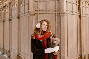 Young woman in winter clothes and fur earmuffs. Girl with teddy bear and mulled wine